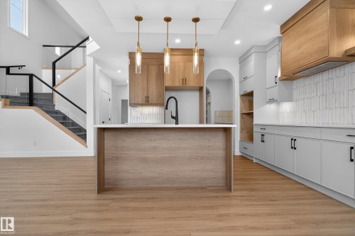 Dual tone kitchen with backsplash, light wood-type flooring, arched walkways, pendant lighting, and a kitchen island with sink - 26 Rosa Crescent, St. Albert, AB - Indoor Photo Showing Kitchen