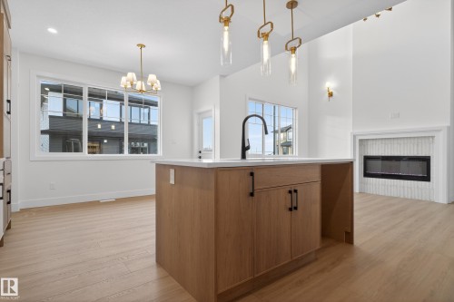 Kitchen with wood finish cabinets, light wood-style floors, suspended lighting, an island with sink, and a glass covered fireplace - 26 Rosa Crescent, St. Albert, AB - Indoor Photo Showing Kitchen