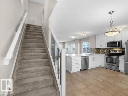 Kitchen featuring stainless steel appliances, white cabinetry, a textured ceiling, tasteful backsplash, and a peninsula - 15 7385 Edgemont Way, Edmonton, AB - Indoor Photo Showing Kitchen