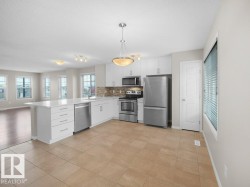 Kitchen featuring stainless steel appliances, white cabinetry, open floor plan, light tile patterned flooring, and a textured ceiling - 