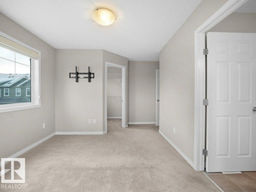 Unfurnished bedroom featuring a walk in closet, light colored carpet, and a textured ceiling - 15 7385 Edgemont Way, Edmonton, AB - Indoor Photo Showing Other Room