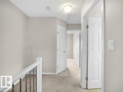 Hallway with an upstairs landing, light colored carpet, and a textured ceiling - 