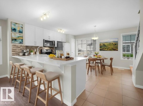 Kitchen with a kitchen bar, a peninsula, white cabinetry, stainless steel appliances, and decorative light fixtures - 15 7385 Edgemont Way, Edmonton, AB - Indoor