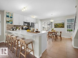Kitchen with a kitchen bar, a peninsula, white cabinetry, stainless steel appliances, and decorative light fixtures - 
