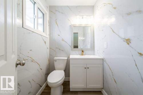 Half bathroom featuring vanity, stone wall, and dark wood-type flooring - 13833 24 Street, Edmonton, AB - Indoor Photo Showing Bathroom