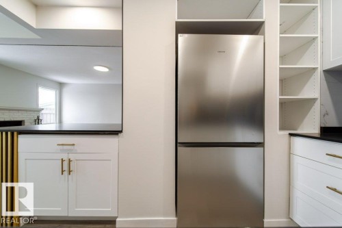 Kitchen featuring freestanding refrigerator, dark countertops, white cabinetry, a fireplace, and open shelves - 13833 24 Street, Edmonton, AB - Indoor