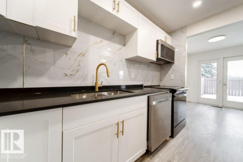Kitchen with white cabinets, stainless steel appliances, light wood-style floors, decorative backsplash, and dark stone countertops - 13833 24 Street, Edmonton, AB - Indoor Photo Showing Kitchen With Double Sink
