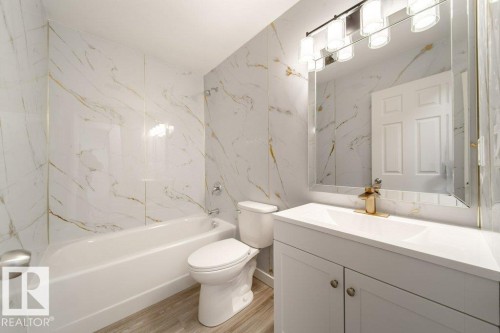 Bathroom featuring vanity, stone wall, washtub / shower combination, and light wood-style floors - 13833 24 Street, Edmonton, AB - Indoor Photo Showing Bathroom