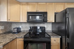 Kitchen featuring black appliances, light wood finish cabinets, decorative backsplash, and dark stone counters - 