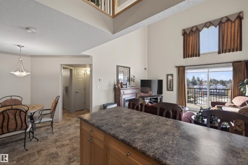 Kitchen with pendant lighting, a high textured ceiling, wood finish cabinetry, open floor plan, and stone finish floors - 427 13005 140 Avenue, Edmonton, AB - Indoor Photo Showing Dining Room