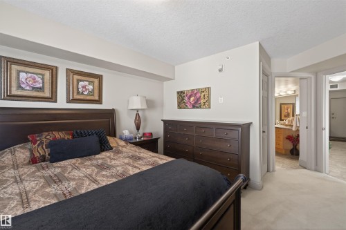Bedroom featuring a closet, a textured ceiling, light carpet, and connected bathroom - 427 13005 140 Avenue, Edmonton, AB - Indoor Photo Showing Bedroom