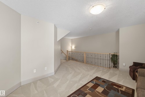 Living area featuring an upstairs landing, a textured ceiling, and light colored carpet - 427 13005 140 Avenue, Edmonton, AB - Indoor Photo Showing Other Room