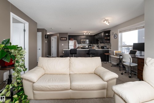 Living area with a desk, light colored carpet, and a textured ceiling - 325 1520 Hammond Gate, Edmonton, AB - Indoor Photo Showing Living Room