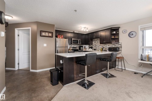 Kitchen featuring a breakfast bar, stainless steel appliances, backsplash, dark wood finish cabinetry, and open shelves - 325 1520 Hammond Gate, Edmonton, AB - Indoor Photo Showing Kitchen