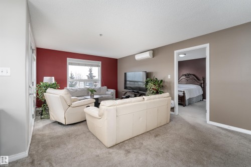 Carpeted living room featuring a textured ceiling and a mini split for heating / cooling - 325 1520 Hammond Gate, Edmonton, AB - Indoor Photo Showing Living Room