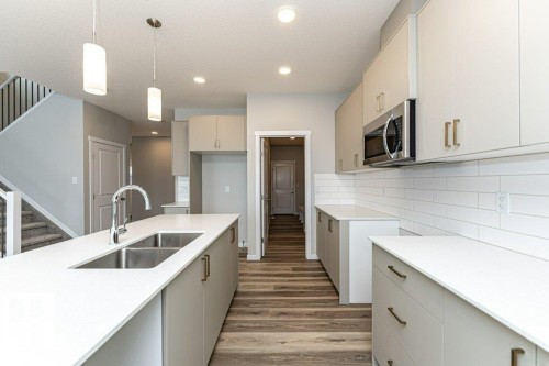Kitchen featuring pendant lighting, stainless steel microwave, light wood-type flooring, and light stone counters - 3949 Wren Loop, Edmonton, AB - Indoor Photo Showing Kitchen With Double Sink With Upgraded Kitchen