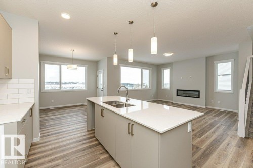 Kitchen with hanging light fixtures, open floor plan, light wood-style floors, a fireplace, and light stone countertops - 3949 Wren Loop, Edmonton, AB - Indoor Photo Showing Kitchen With Double Sink With Upgraded Kitchen