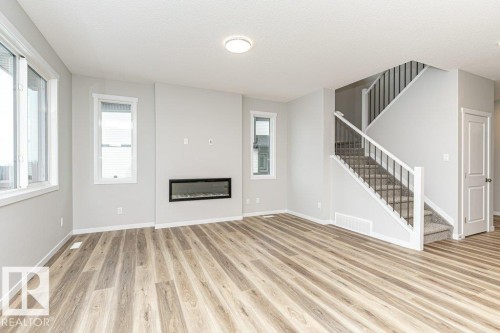 Unfurnished living room featuring light wood-style floors, a glass covered fireplace, and a textured ceiling - 3949 Wren Loop, Edmonton, AB - Indoor With Fireplace