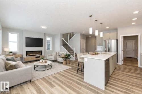 Kitchen with open floor plan, a kitchen island with sink, pendant lighting, a kitchen breakfast bar, and light wood-style flooring - 3949 Wren Loop, Edmonton, AB - Indoor With Fireplace