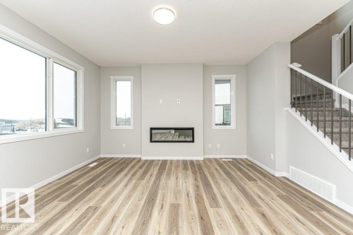 Unfurnished living room featuring a glass covered fireplace and light wood finished floors - 3949 Wren Loop, Edmonton, AB - Indoor With Fireplace