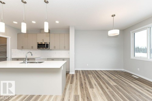 Kitchen featuring pendant lighting, stainless steel microwave, light wood-style flooring, tasteful backsplash, and gray cabinets - 3949 Wren Loop, Edmonton, AB - Indoor Photo Showing Kitchen With Double Sink With Upgraded Kitchen