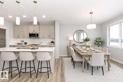 Kitchen with decorative light fixtures, light wood finished floors, an island with sink, stainless steel microwave, and a kitchen breakfast bar - 3949 Wren Loop, Edmonton, AB - Indoor