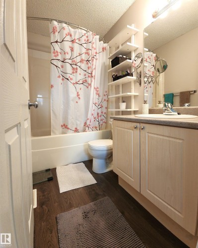 Full bathroom featuring vanity, shower / bath combination with curtain, a textured ceiling, and dark wood finished floors - 5424 204 Street, Edmonton, AB - Indoor Photo Showing Bathroom