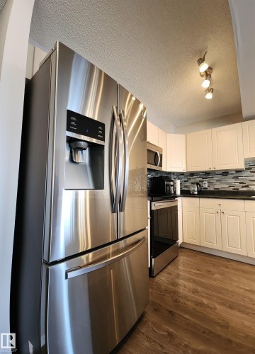 Kitchen featuring stainless steel appliances, dark countertops, a textured ceiling, tasteful backsplash, and white cabinetry - 5424 204 Street, Edmonton, AB - Indoor Photo Showing Kitchen With Stainless Steel Kitchen