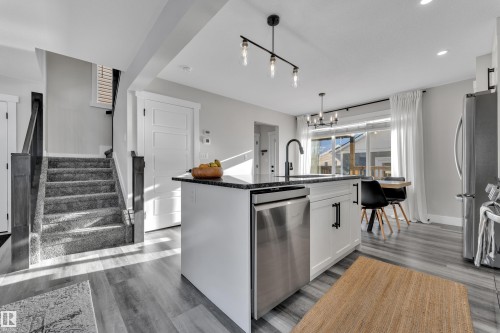 Kitchen with white cabinets, dark stone countertops, a center island with sink, and stainless steel appliances - 7613 16 Av Sw, Edmonton, AB - Indoor Photo Showing Kitchen With Upgraded Kitchen