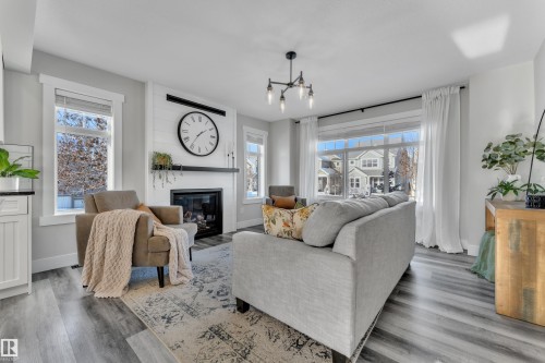 Living room featuring wood finished floors, a large fireplace, and suspended lighting - 7613 16 Av Sw, Edmonton, AB - Indoor Photo Showing Living Room With Fireplace