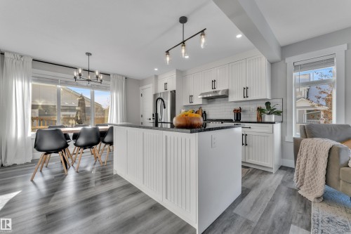 Kitchen with white cabinetry, a chandelier, dark stone countertops, and a kitchen island with sink - 7613 16 Av Sw, Edmonton, AB - Indoor Photo Showing Kitchen With Upgraded Kitchen