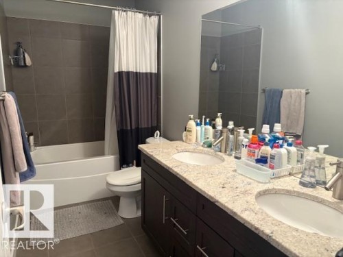 Bathroom featuring double vanity, shower / bath combo with shower curtain, and dark tile patterned flooring - 867 Armitage Wynd Sw, Edmonton, AB - Indoor Photo Showing Bathroom