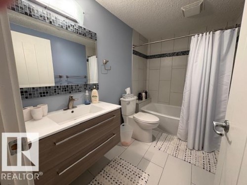 Large basement bathroom featuring vanity, a textured ceiling, shower / bath combination with curtain, tasteful backsplash, and light tile patterned floors - 867 Armitage Wynd Sw, Edmonton, AB - Indoor Photo Showing Bathroom