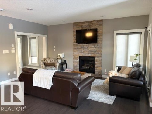 Living room featuring a stone fireplace, dark wood finished floors, and a textured ceiling - 867 Armitage Wynd Sw, Edmonton, AB - Indoor Photo Showing Living Room With Fireplace