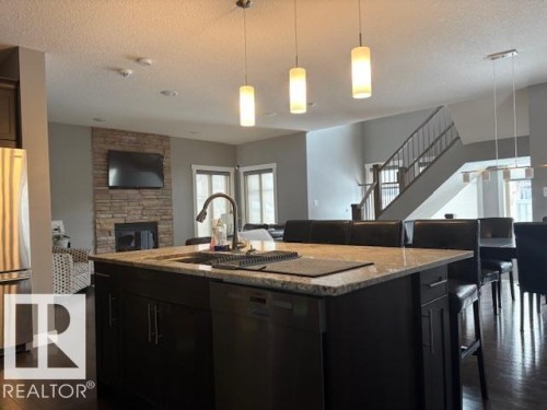 Kitchen with pendant lighting, open floor plan, light stone countertops, dark cabinetry, and a textured ceiling - 867 Armitage Wynd Sw, Edmonton, AB - Indoor Photo Showing Kitchen