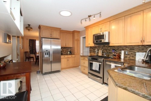 Kitchen featuring stainless steel appliances, light wood finish cabinets, dark stone countertops, and light tile patterned floors - 2812 35 Street Nw, Edmonton, AB - Indoor Photo Showing Kitchen With Double Sink