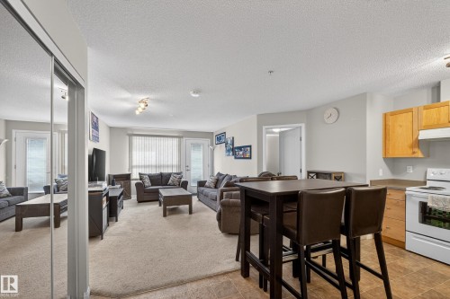 Kitchen featuring white electric range oven, a textured ceiling, light carpet, light countertops, and open floor plan - 131 1520 Hammong Gate, Edmonton, AB - Indoor Photo Showing Kitchen