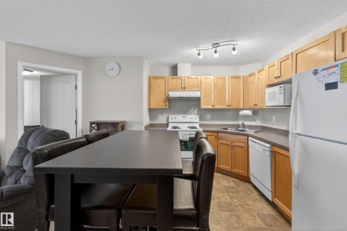 Kitchen featuring white appliances, a textured ceiling, and light wood finish cabinetry - 131 1520 Hammong Gate, Edmonton, AB - Indoor Photo Showing Kitchen With Double Sink