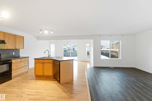 Kitchen with open floor plan, dark countertops, black range with electric cooktop, backsplash, and light wood-type flooring - 4507 164A Avenue, Edmonton, AB - Indoor Photo Showing Kitchen With Double Sink