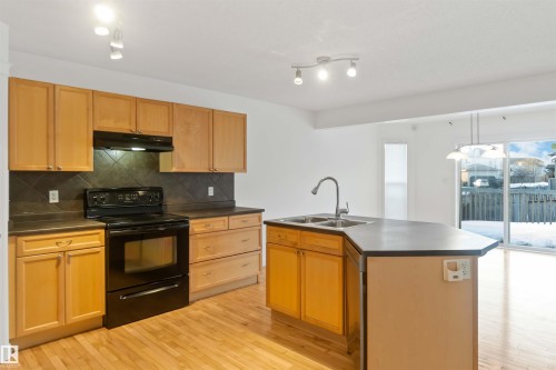 Kitchen featuring black electric range oven, light wood finished floors, dark countertops, and an island with sink - 4507 164A Avenue, Edmonton, AB - Indoor Photo Showing Kitchen With Double Sink