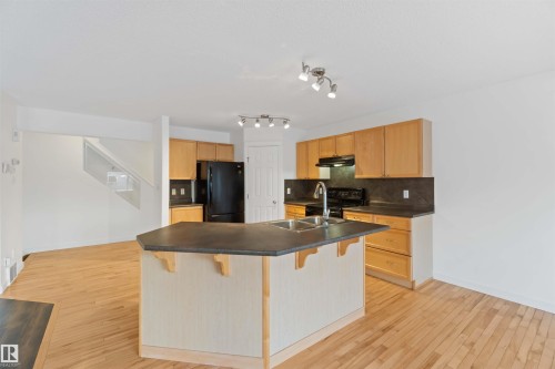 Kitchen with tasteful backsplash, a breakfast bar area, black appliances, and light wood-type flooring - 4507 164A Avenue, Edmonton, AB - Indoor Photo Showing Kitchen With Double Sink
