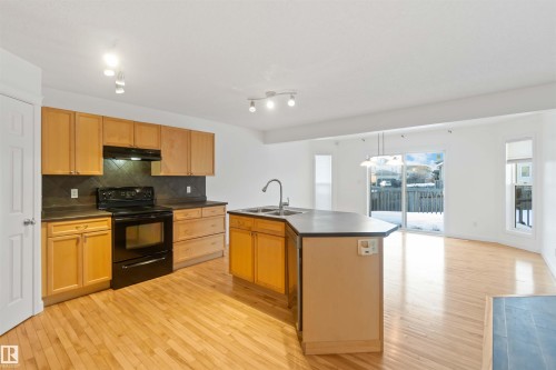 Kitchen with black electric range, dark countertops, a center island with sink, light wood-style floors, and tasteful backsplash - 4507 164A Avenue, Edmonton, AB - Indoor Photo Showing Kitchen With Double Sink