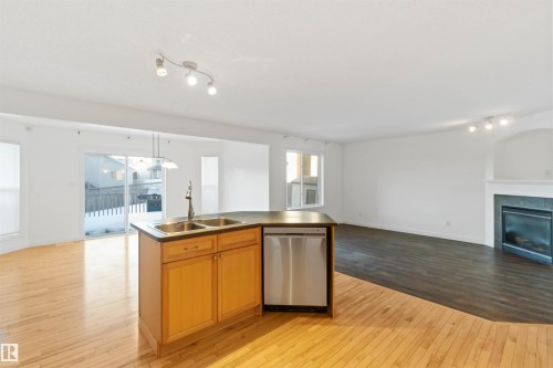 Kitchen featuring open floor plan, light wood-type flooring, dishwasher, a tile fireplace, and wood finish cabinetry - 4507 164A Avenue, Edmonton, AB - Indoor Photo Showing Kitchen With Fireplace With Double Sink