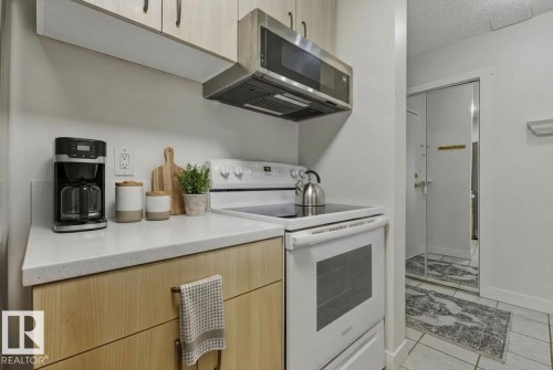 Kitchen with light wood finish cabinetry, white electric stove, stainless steel microwave, modern cabinets, and a textured ceiling - #117 5005 31 Avenue, Edmonton, AB - Indoor Photo Showing Kitchen