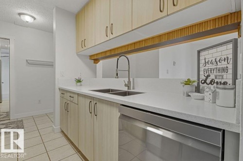 Kitchen with stainless steel dishwasher, light wood finish cabinets, a textured ceiling, light stone countertops, and light tile patterned floors - #117 5005 31 Avenue, Edmonton, AB - Indoor Photo Showing Kitchen With Double Sink