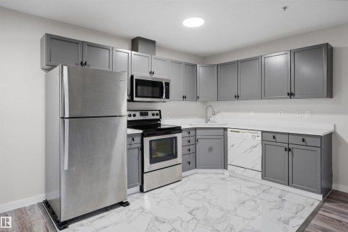Unfurnished living room featuring a tile fireplace, wooden walls, and light wood-style flooring - 115 2098 Blackmud Creek Drive, Edmonton, AB - Indoor With Fireplace