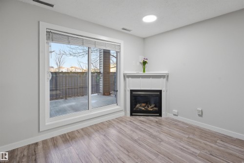 Unfurnished living room featuring light wood-style flooring and a glass covered fireplace - 115 2098 Blackmud Creek Drive, Edmonton, AB - Indoor Photo Showing Other Room With Fireplace
