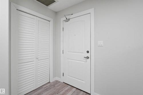 Laundry area with a paneled ceiling, stacked washer / dryer, and wood finished floors - 115 2098 Blackmud Creek Drive, Edmonton, AB - Indoor Photo Showing Laundry Room