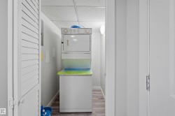 Laundry area with a paneled ceiling, stacked washer / dryer, and wood finished floors - 