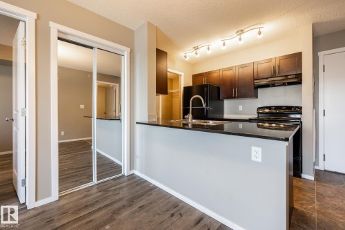 Kitchen with range with electric cooktop, dark stone counters, a peninsula, freestanding refrigerator, and a textured ceiling - 433 3315 James Mowatt Trail, Edmonton, AB - Indoor Photo Showing Kitchen